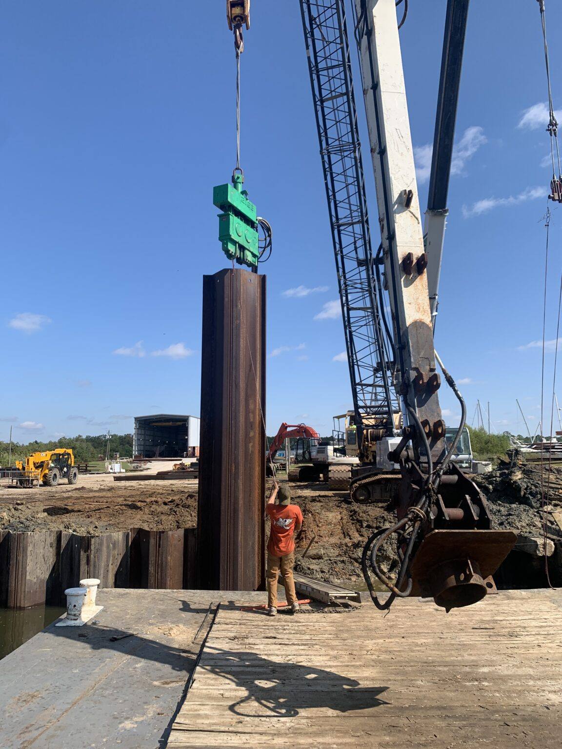 Crane holding a vibratory hammer over a steel sheet pile while a crew member guides it