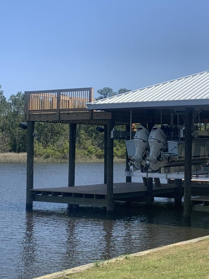Boathouse with boats on lifts and a sun deck above, seen from the water side