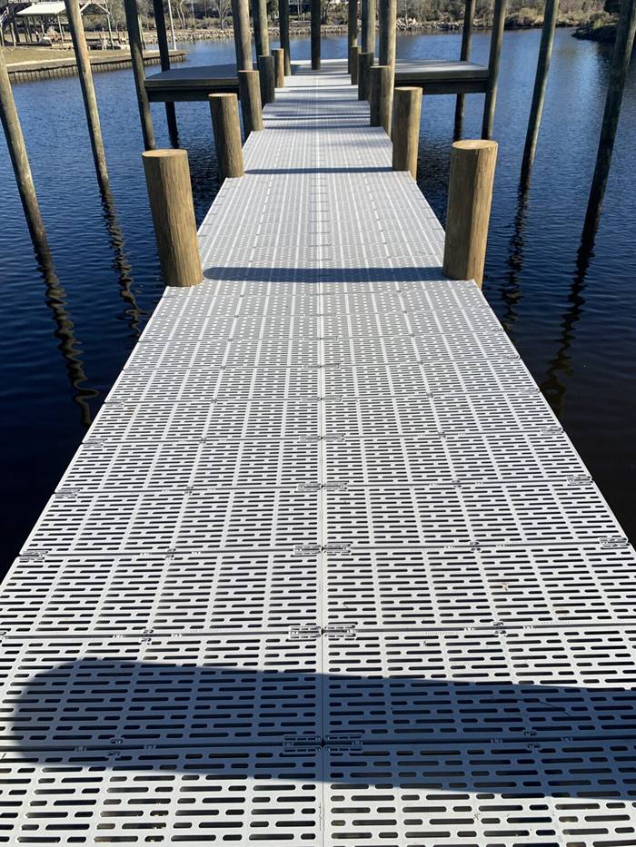 Pier decked with light gray grated panels between pilings
